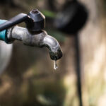 Old faucet with water leaking drop to the ground.